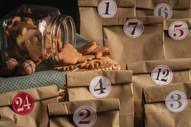 Overturned glass jar full with gingerbread Christmas cookies surrounded by numbered paper bags, a selfmade advent calendar.