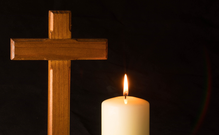 Burning candle and cross in a cemetery against black background.