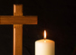 Burning candle and cross in a cemetery against black background.