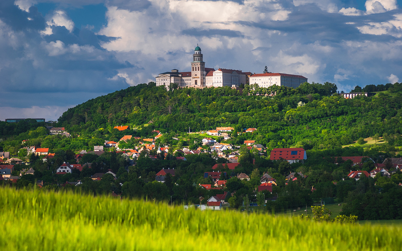 Pannonhalma Archabbey and early summer wheat field with cloudy sky, Hungary.