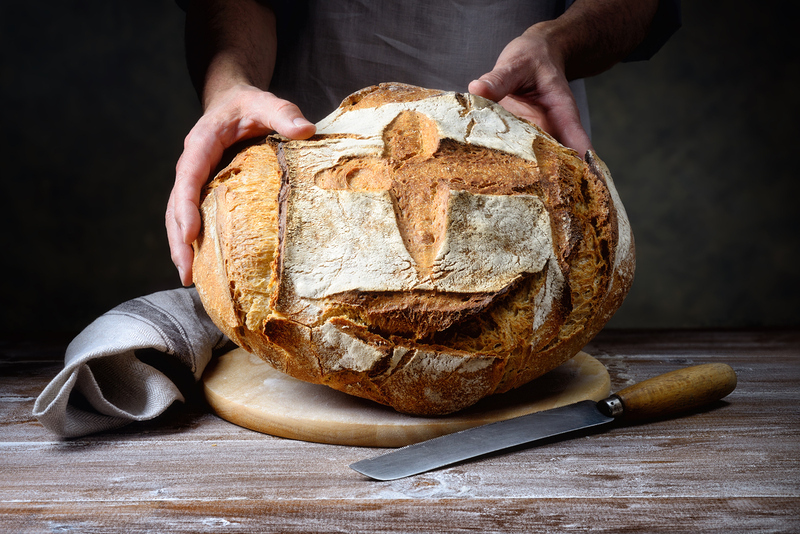 Hände halten einen Laib Brot mit Kreuz.